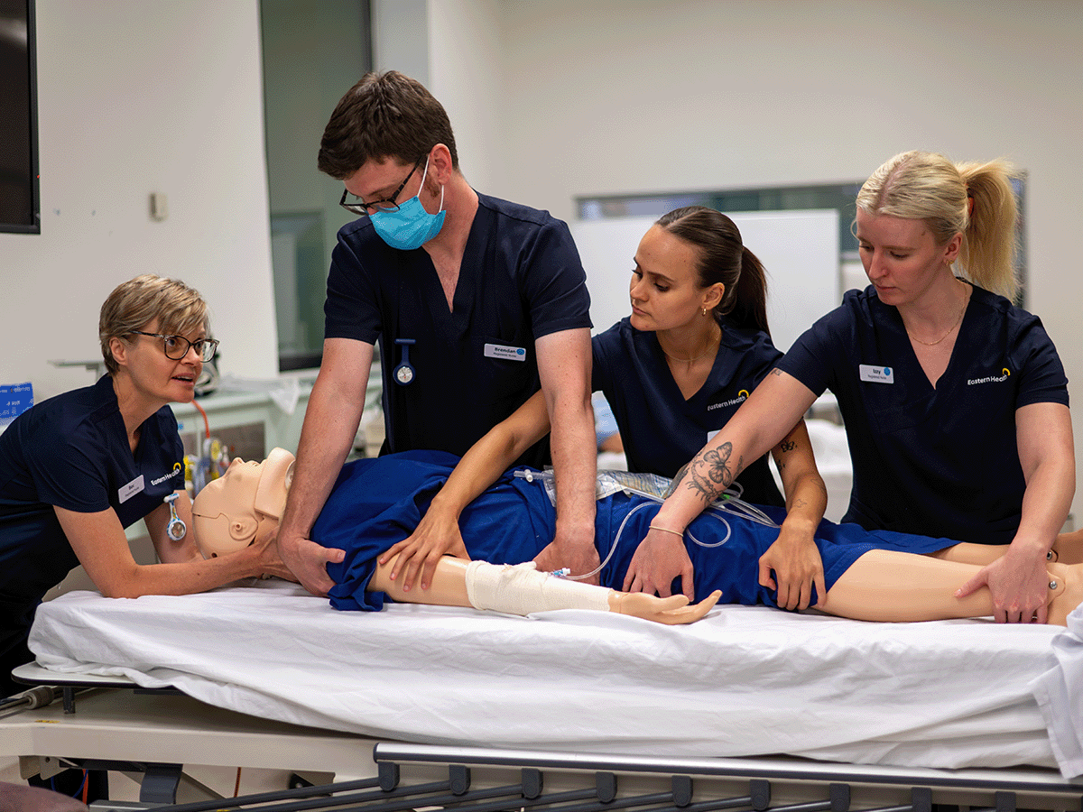 Several nurses rotate a simulated patient in a hospital bed.